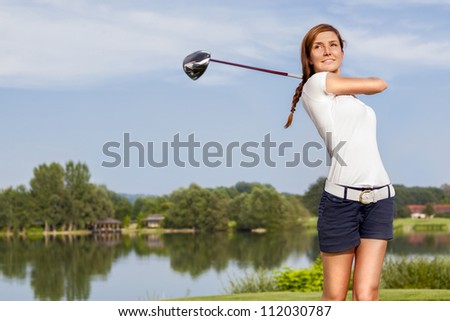 Girl golf player teeing off with driver from tee box, front view.