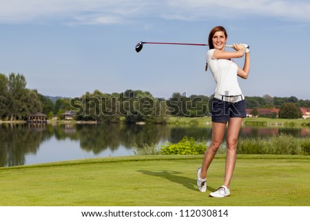 Girl golf player teeing-off with driver from tee-box, front view.