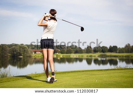 stock-photo-girl-golf-player-with-driver-teeing-off-from-tee-box-to-shoot-over-lake-view-from-behind-112030817.jpg