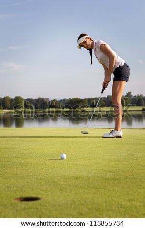 Woman golf player putting ball on green. Golf ball rolling towards cup.