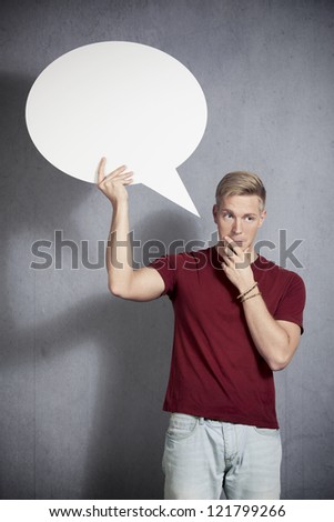 Serious man thinking while holding white empty speech balloon with space for text isolated on grey background.