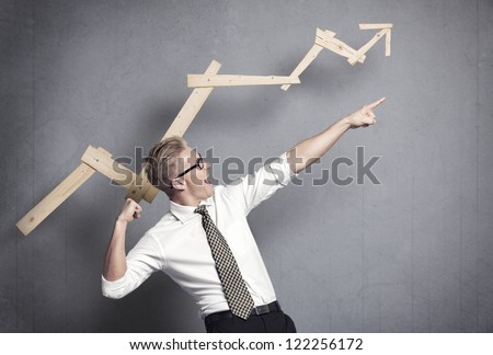 Concept: Successful business trend. Happy talented businessman pointing arm upwards in front of ascending business graph, isolated on grey background.