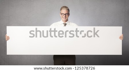 Friendly businessman holding white blank horizontal billboard with space for text isolated on grey background.