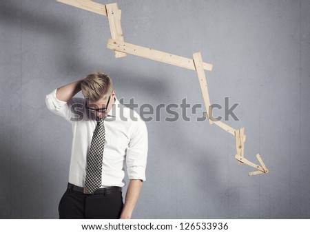 Concept: Business failure. Young worried businessman in front of business graph with negative trend, isolated on grey background.