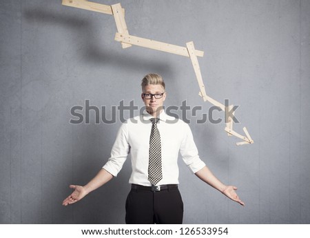 Concept: Business decline. Young displeased businessman in front of business graph pointing down, isolated on grey background.