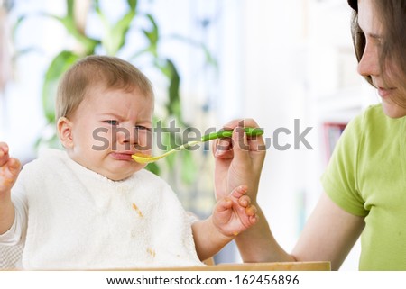 Crying Baby Boy Refusing To Eat Food From Spoon With Hands Dirty Of Vegetable Puree.