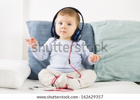 Adorable baby boy listening music at earphones while holding his hands in the air like a conductor.