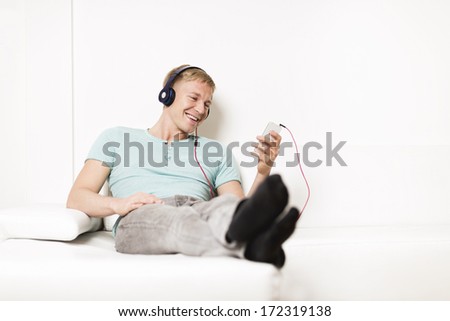 Young happy man listening to music with earphones and smartphone while relaxing on sofa.