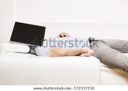 Sleeping man lying on sofa with a grey book covering his face, on white background.