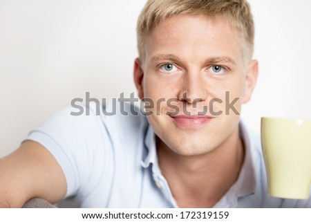 Close-up portrait of smiling happy man with blue eyes  enjoying a cup of coffee and looking straight.