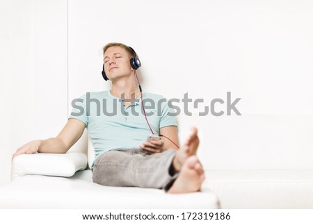 Relaxed young man listening to music with headset and smartphone while relaxing on sofa with eyes closed.