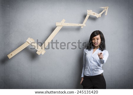 Concept: Successful career or business. Young confident businesswoman pointing finger in front of ascending business chart, isolated on grey background.