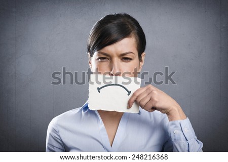 Unhappy young businesswoman holding empty white card with space for text in front of her mouth, isolated on grey background.