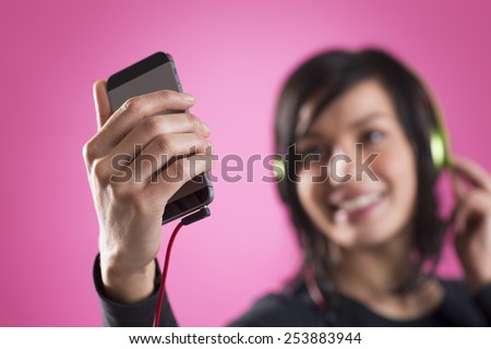 Smiling happy girl enjoying listening to music with headphones and mp3 player, isolated on pink background.
