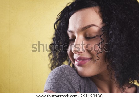 Smiling woman being happy and confident, looking with half closed eyes to the left onto her shoulder, isolated on yellow background with empty copy space.