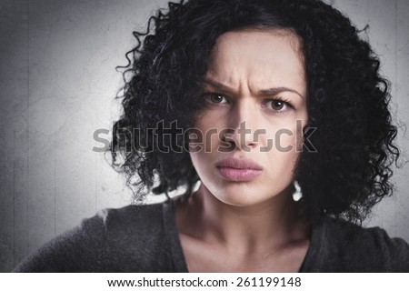 Closeup portrait of a frowning woman, being angry and mad, isolated on grey background.