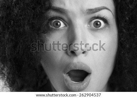 Black and white close up of a frightened astonished woman with wide opened eyes and dramatic look.