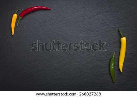 Four colorful chili peppers isolated on a slate stone slab with empty copy space.