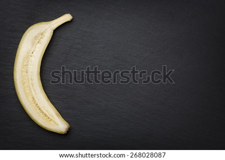 One half of a sliced banana, looking noble, isolated on dark stone slab with empty copyspace.