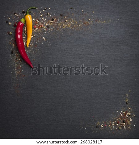 Two hot chili peppers with different spices on a dark stone slab with copyspace.