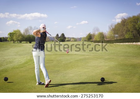 Woman golf player teeing off ball.