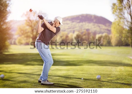 Senior golf player teeing off with golf club at sunset.