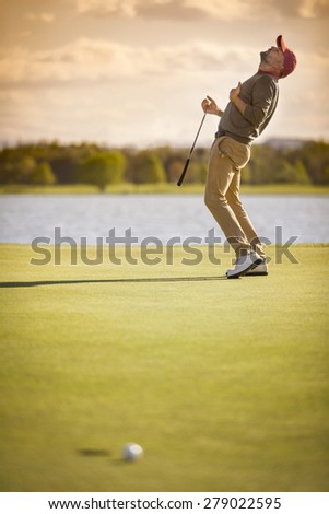 Male golf player showing emotion after ball missing hole at sunset.