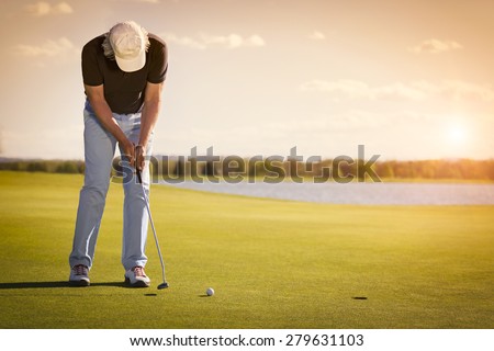 Male senior golf player putting on green at beautiful sunset, with empty copyspace.