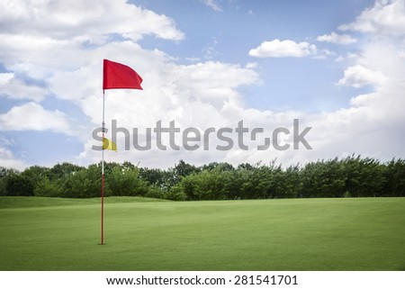 Red golf flag on green fairway with beautiful blue sky, with empty copyspace.