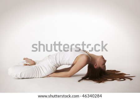 Young lady practicing yoga in lotus fish posture (Matsyasana) in white clothes with red hair spread out on white background, high-key image.