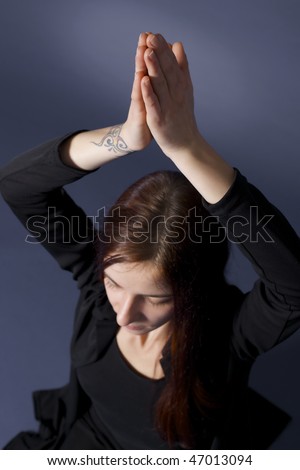 Top view of young lady practicing yoga in Siddhasana posture with eyes closed in black clothes on blue background.