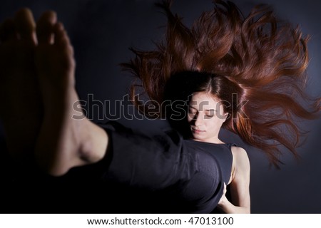 Young lady practicing yoga in shoulder stand posture (Sarvangasana) in black clothes with red hair spread out on dark background, high-key image.
