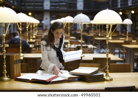 Young confident woman standing at desk in old university library studying books.