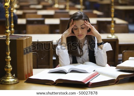 Young pretty student sitting at desk in old university library studying books.