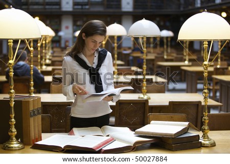 Young confident student standing at desk in old university library studying books.