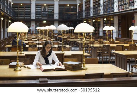 Attractive student sitting at desk in old university library studying books.