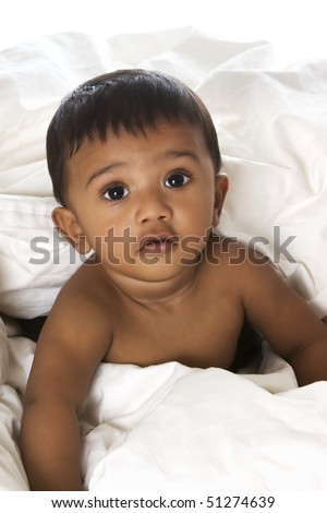 Adorable Indian baby lying on floor covered by a soft blanket and peeping out, isolated on white background.