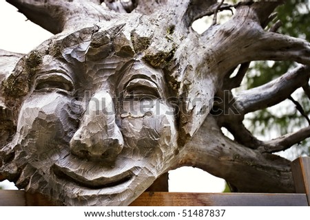 Wooden smiling face carved out of tree trunk with roots as hair.