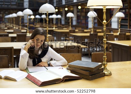 Young attractive student sitting at desk in old university library studying books.