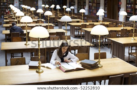 Attractive student sitting at desk in old university library and studying books.