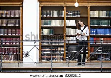 Young attractive woman standing in front of bookshelf in old university library reading a book.