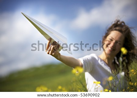 Jolly woman in green field holding up a paper plane into the blue sky expressing liberation.