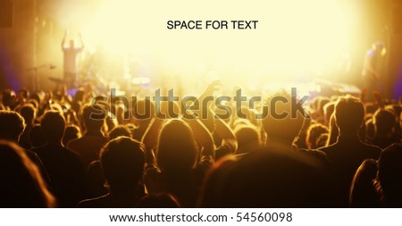 Orange-toned image of audience at live concert cheering with bright light at stage area as free space for text.