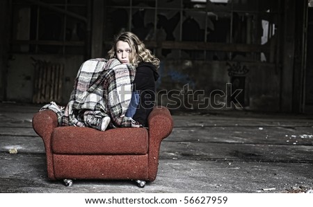 Sad girl sitting in shabby red sofa being covered with old blanket.