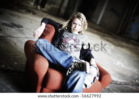 Cool girl sitting relaxed in shabby red sofa in old factory hall.