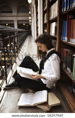 Female student sitting at bookshelf in old library reading books.