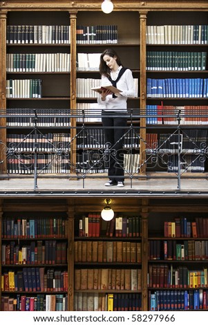 Attractive female student standing in front of bookshelf in old university library reading a book.