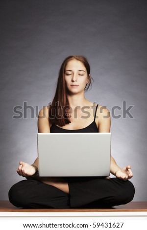 Balance in at work: Young pretty woman sitting in lotus posture on floor with laptop on her lap, backlit grey background.