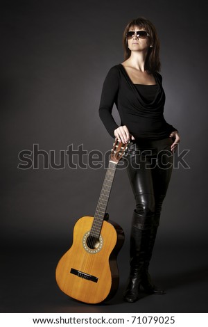 Full-body portrait of glamorous young woman in black posing with guitar on floor, isolated on black background.