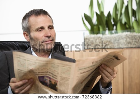 Handsome business executive sitting in office chair reading newspaper.